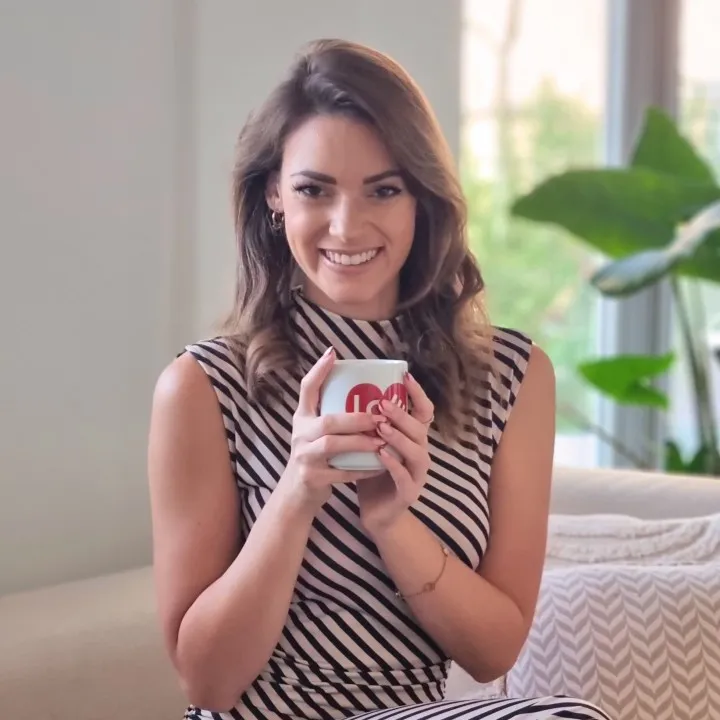 Porträt einer lächelnden Frau in einem gestreiften Kleid namens Nadine Schambach von Design Nook, die eine Tasse hält, Partnerin eines Startups für nachhaltige Farben namens Mynt aus Deutschland, in einem gemütlichen und modernen Innenraum.