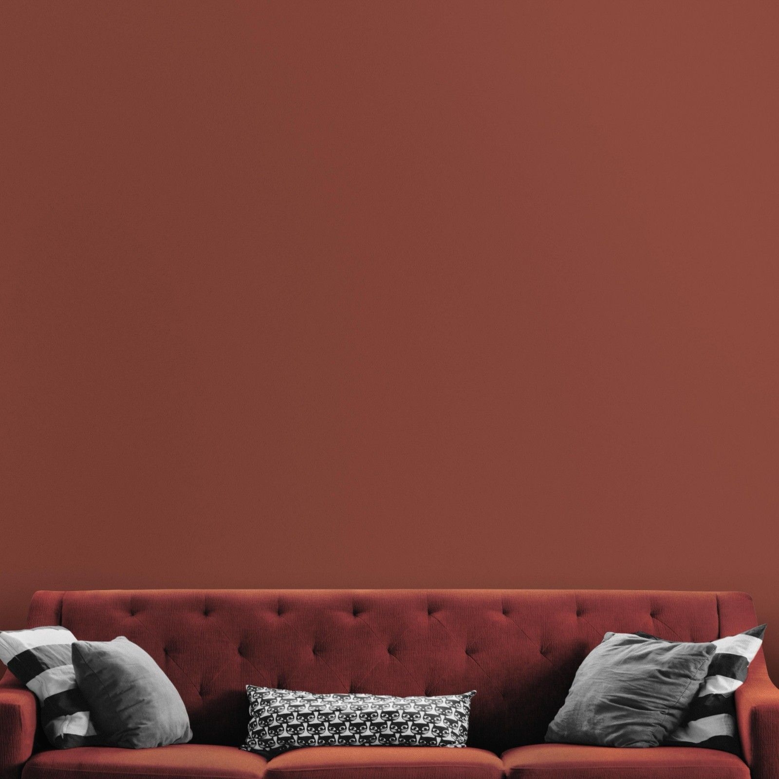 Dunkelrote Wandfarbe Kiss Me Now nachhaltig von Mynt vor rotem Sofa und grauen Pölstern.