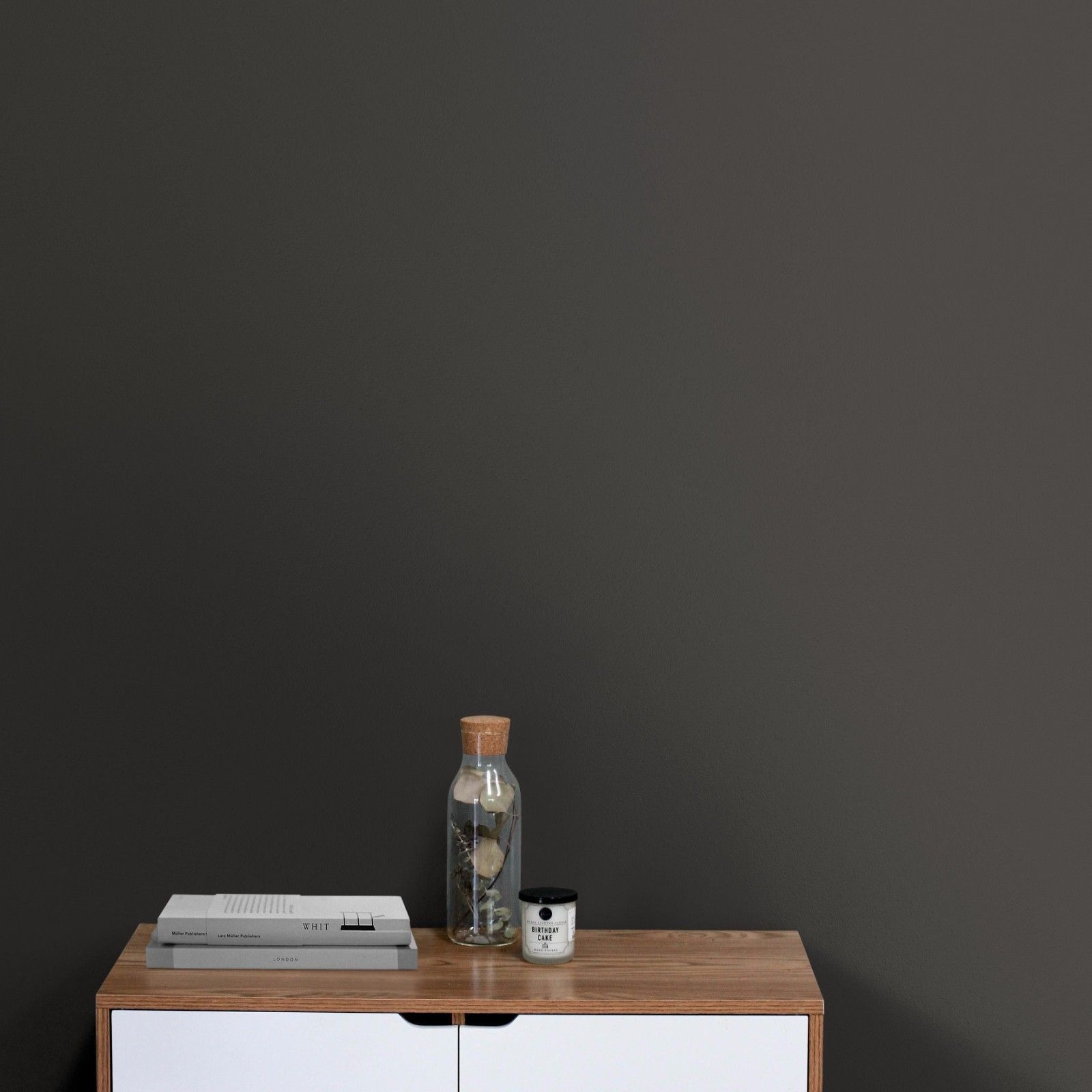 Schwarze nachhaltige Wandfarbe Talk Dirty von Mynt mit einem Holzmöbel mit weißen Laden und einer Glasflasche.