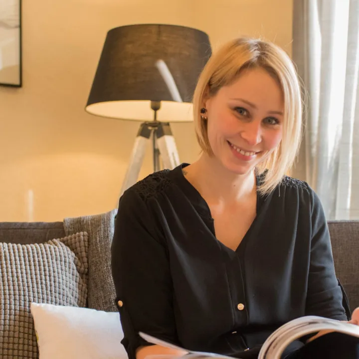Porträt einer lächelnden Frau namens Carolin Richter von Wohnjuwel Home Staging, die auf einem Sofa sitzt und ein Magazin liest, Partnerin eines Startups für nachhaltige Farben namens Mynt aus Deutschland, in einem gemütlich eingerichteten Raum.