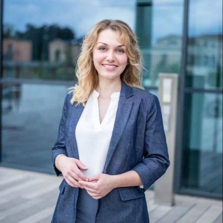 Porträt einer lächelnden Frau in einem blauen Blazer von Emotionrooms Home Staging & Redesign vor einem modernen Gebäude, Partnerin eines Startups für nachhaltige Farben namens Mynt aus Deutschland.